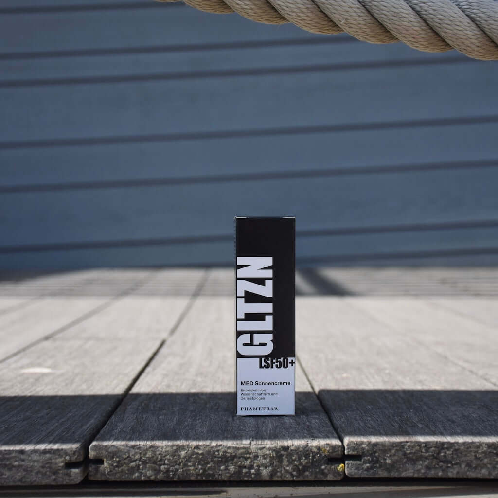 GLTZN Sonnencreme LSF50+ steht präsent auf einem Holzbrett.
