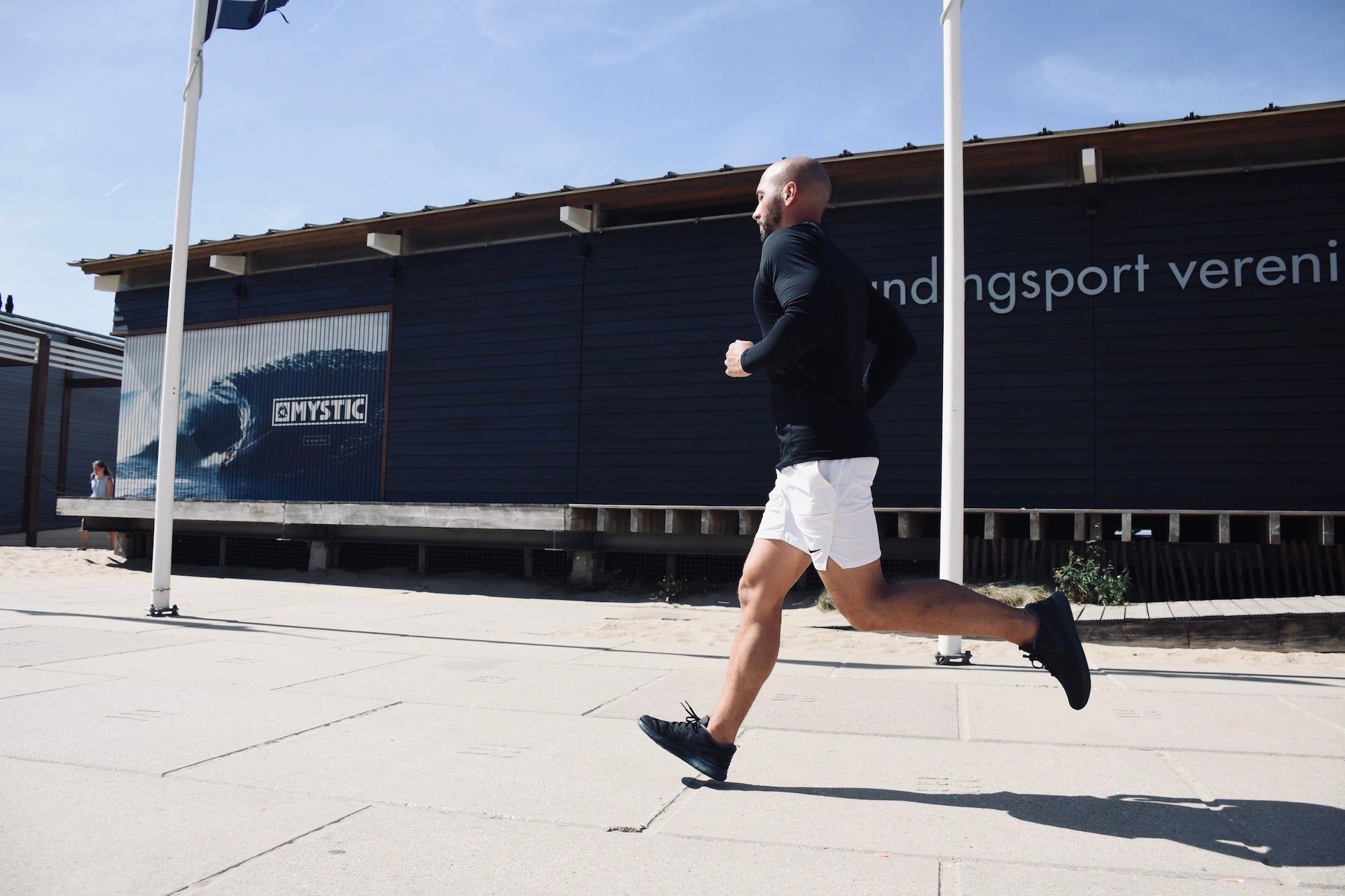 Mann mit Glatze joggt in der Sonne auf Asphalt mit Gebäuden im Hintergrund