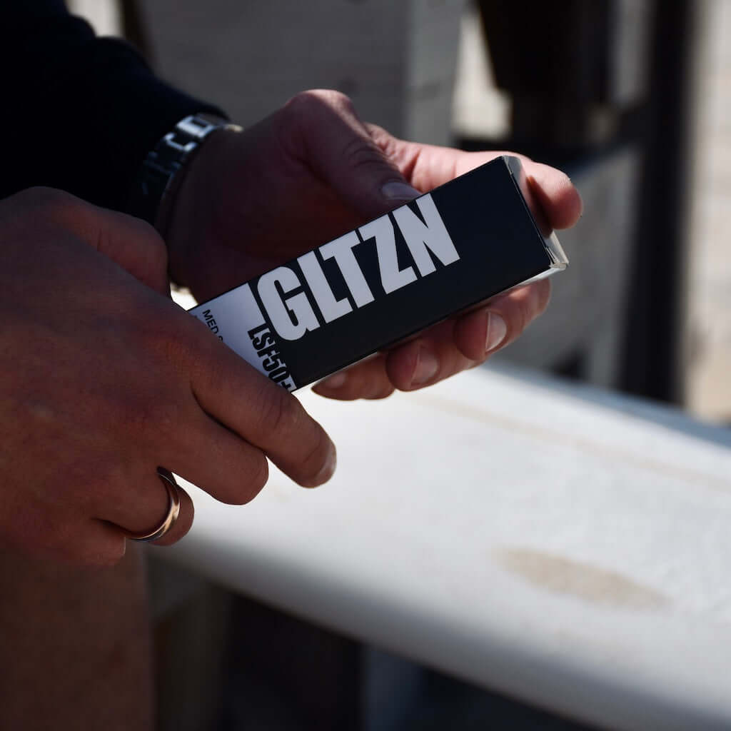 Zwei Männerhände halten die schwarz weiße Verpackung von GLTZN Med Sonnencreme