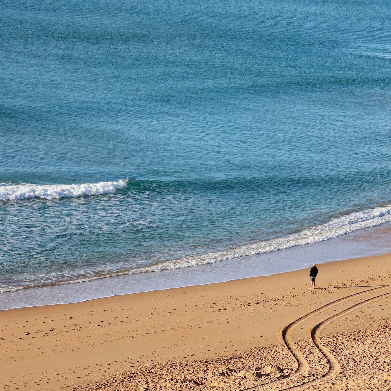 Mann mit Glatze und schwarzem Pulli steht am Strand