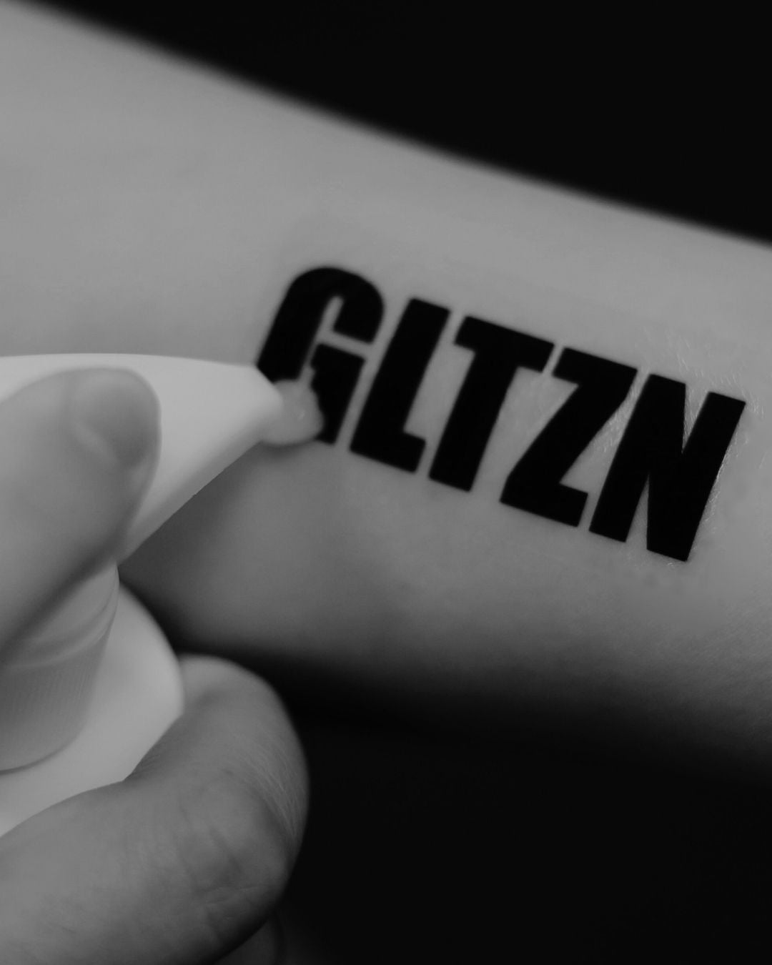 Ein Arm mit GLTZN-Tattoo, auf den gerade Waschgel aufgetragen wird.